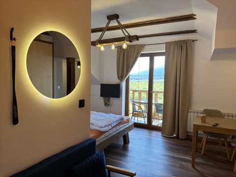 Studio with a double bed, wall TV, backlit round mirror and balcony door with a mountain view