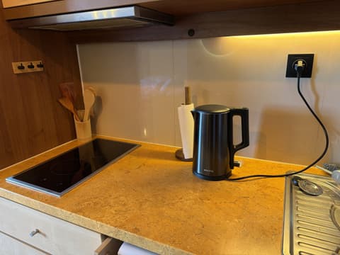 Close-up of the two-zone hob, kettle and wooden cooking utensils under warm cabinet lighting
